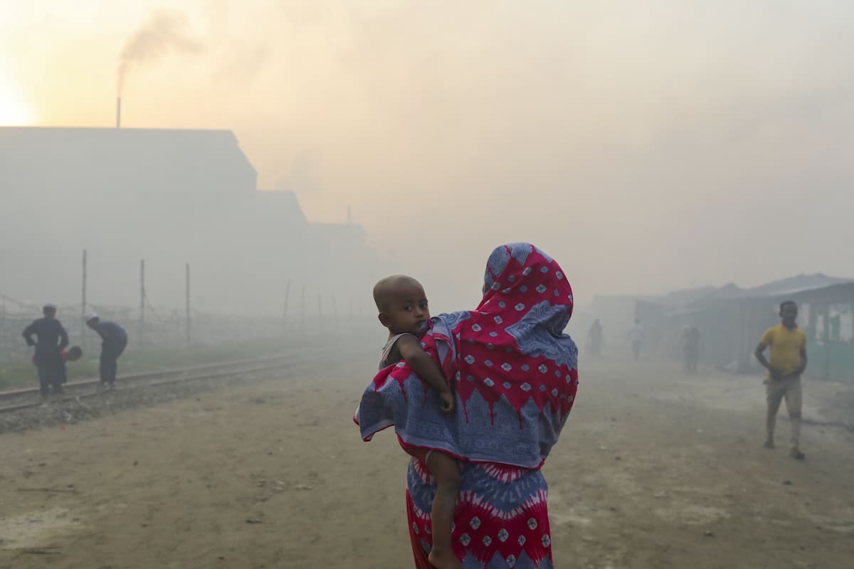 A woman holds a child as smoke rises from a re-rolling mill in Dhaka, Bangladesh